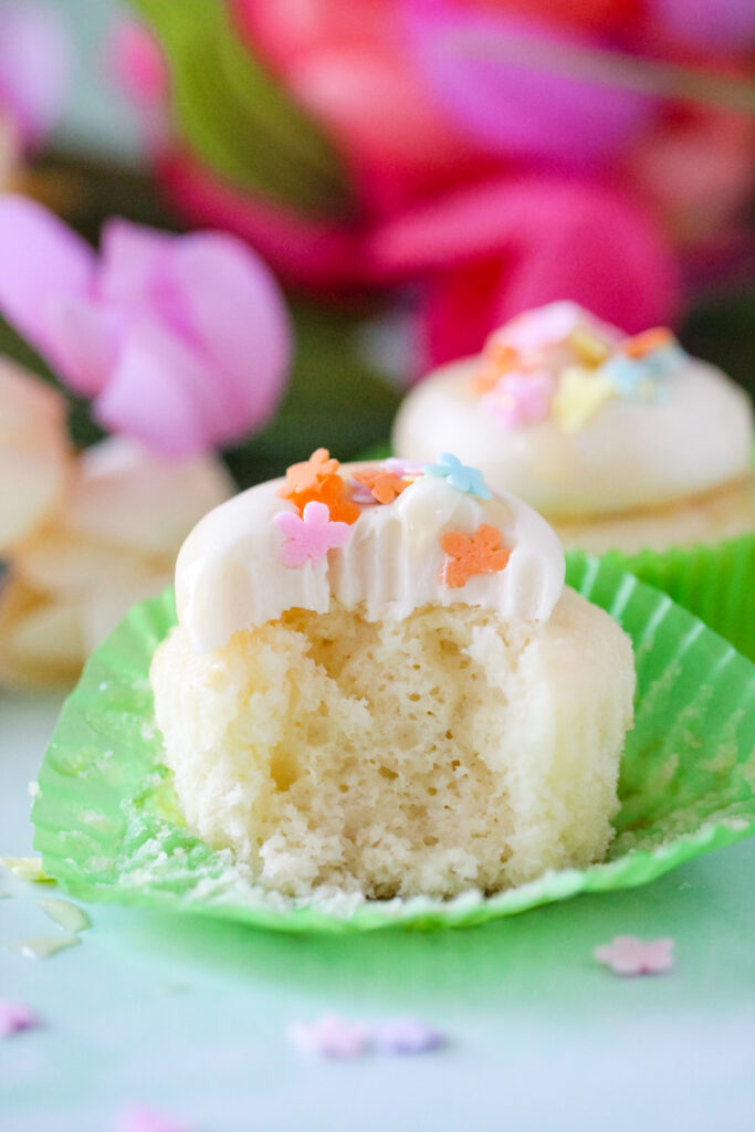 Almond cupcakes topped with honey cream cheese frosting, spring sprinkles, and a drizzle of golden honey on a white plate.