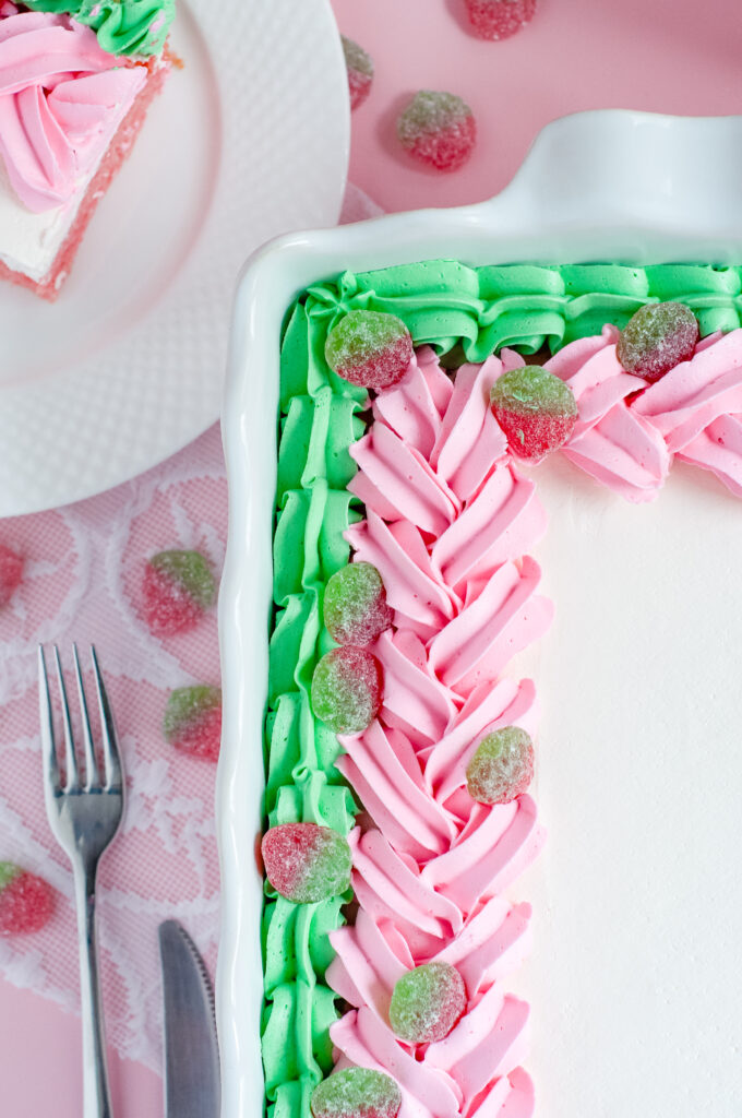 Decorated sheet cake with pink and green piped buttercream and sour strawberry candies, inspired by strawberry soda and vintage candy shop themes.