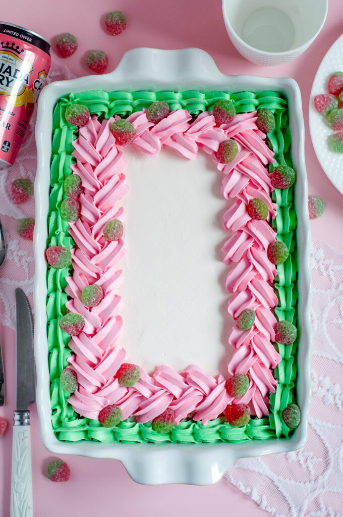 Decorated sheet cake with pink and green piped buttercream and sour strawberry candies, inspired by strawberry soda and vintage candy shop themes.