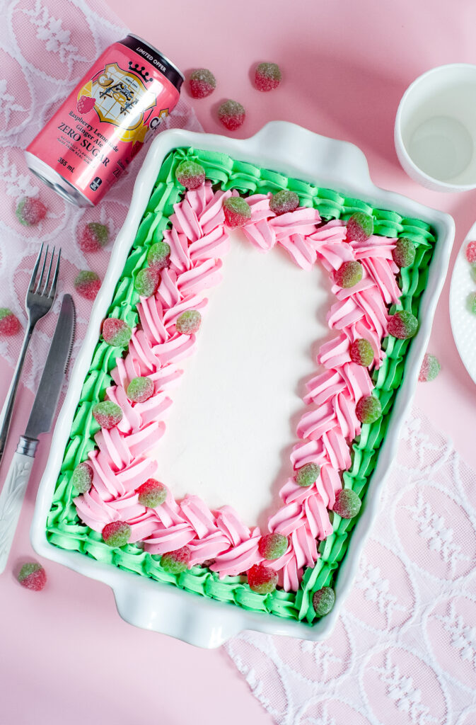 Decorated sheet cake with pink and green piped buttercream and sour strawberry candies, inspired by strawberry soda and vintage candy shop themes.