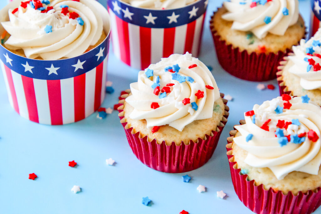 A batch of Patriotic Cupcakes perfect for Fourth of July with patriotic sprinkles on top of the frosting in a festive patriotic cupcake liners.