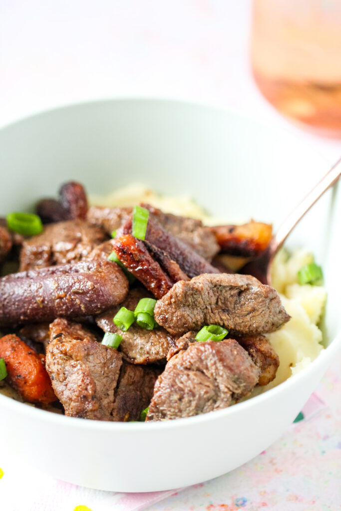 A bowl of garlic butter beef bites on top of mashed potatoes with carrots.