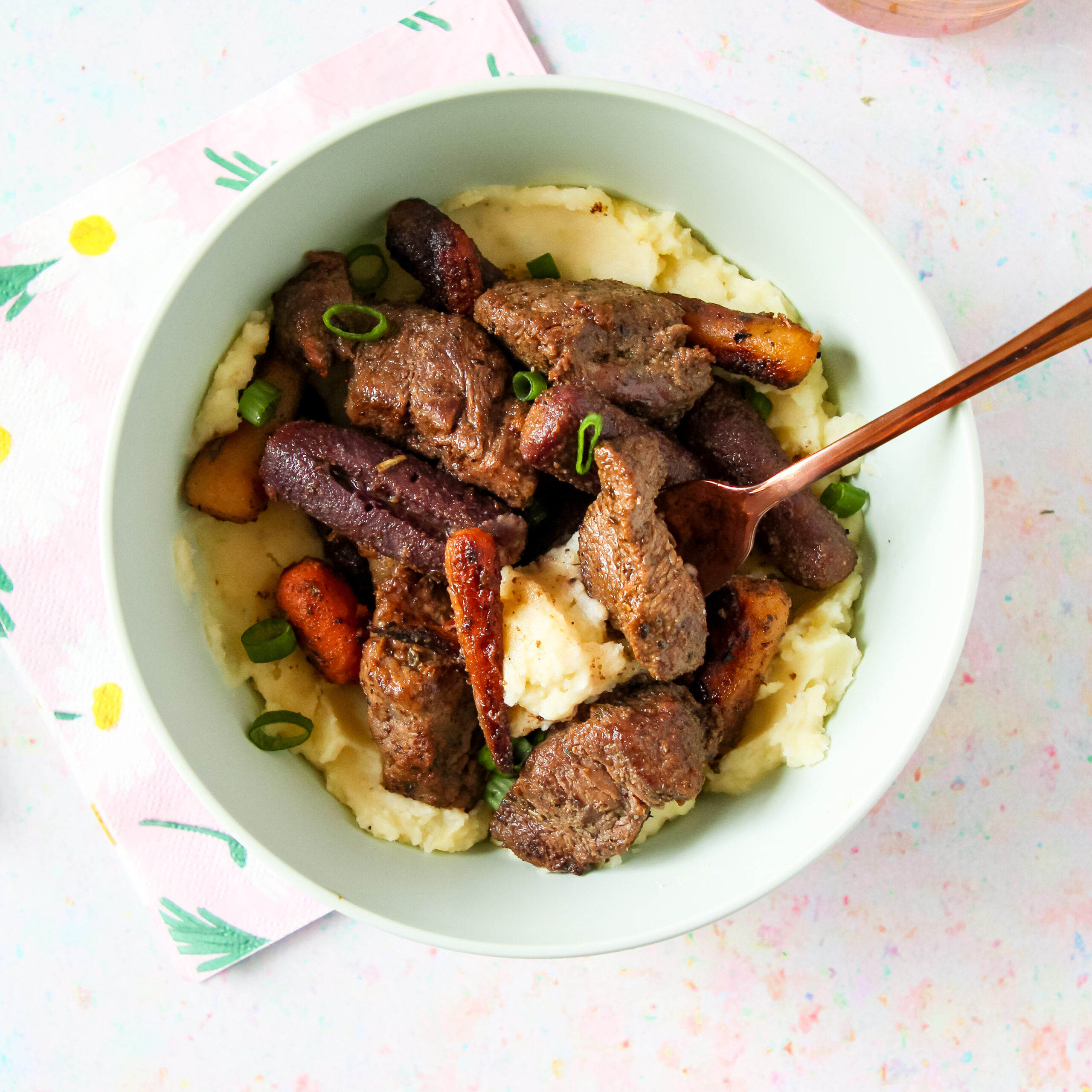 A bowl of garlic butter beef bites on top of mashed potatoes with carrots.