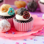 A chocolate cupcake with whipped vanilla donut frosting and donut decorations on top.