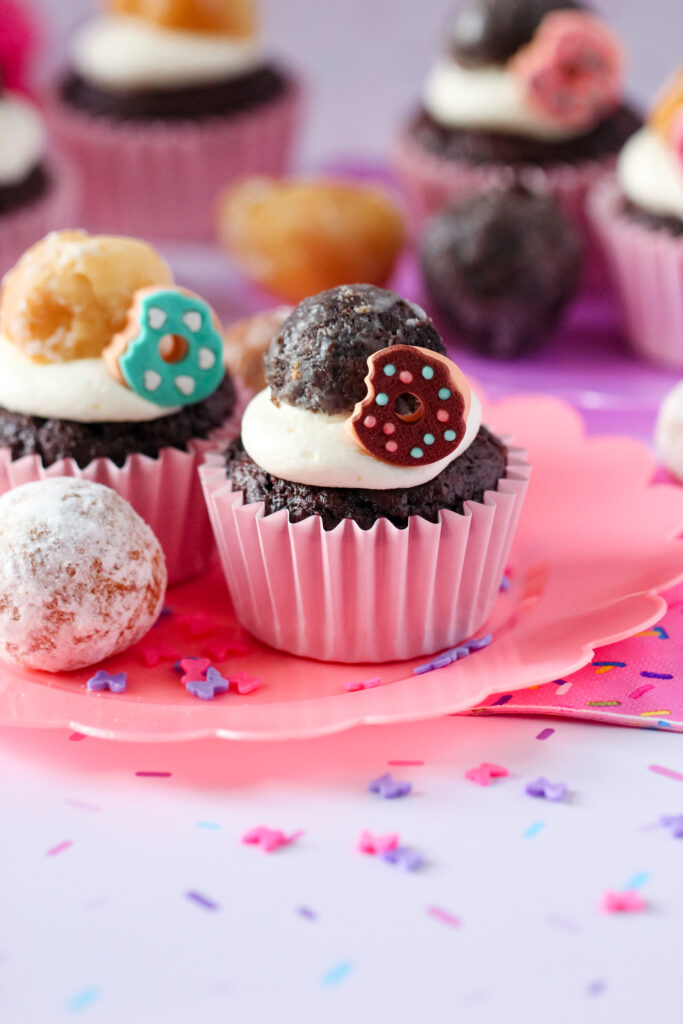 A chocolate cupcake with whipped vanilla donut frosting and donut decorations on top.