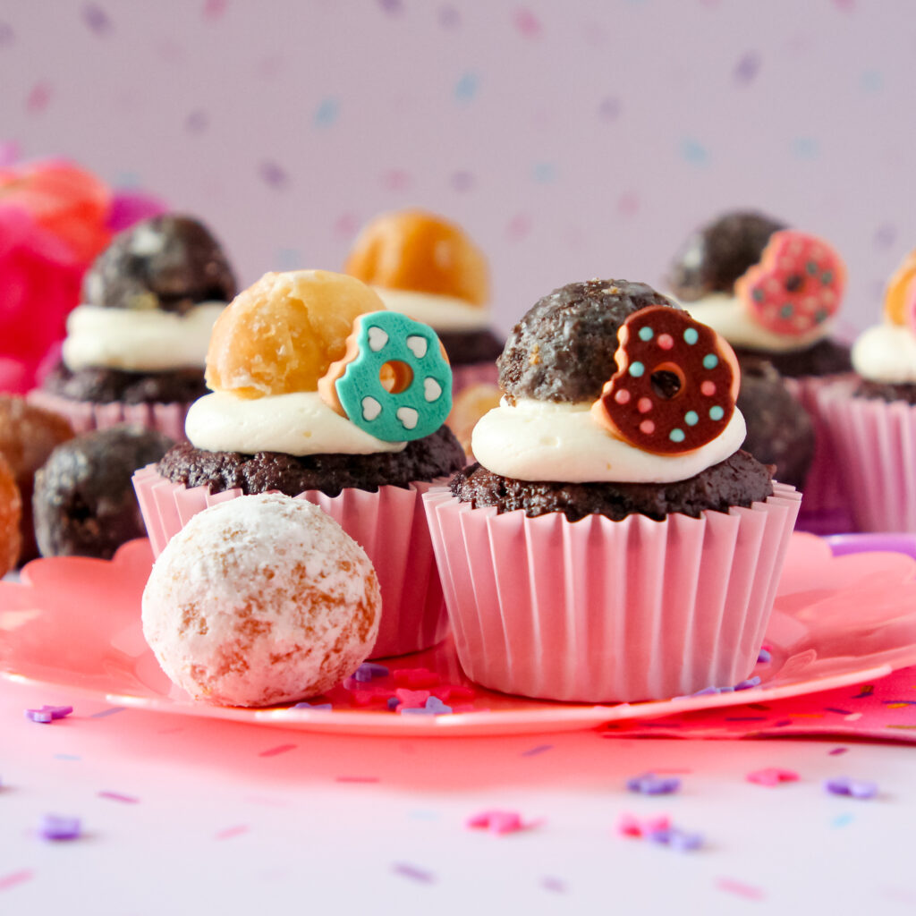 A chocolate cupcake with whipped vanilla donut frosting and donut decorations and munchkin donuts on top.