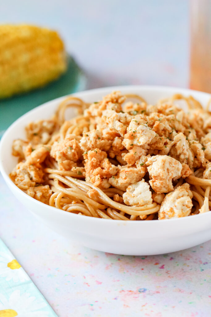A bowl of seasoned ground chicken breast on top of pasta.