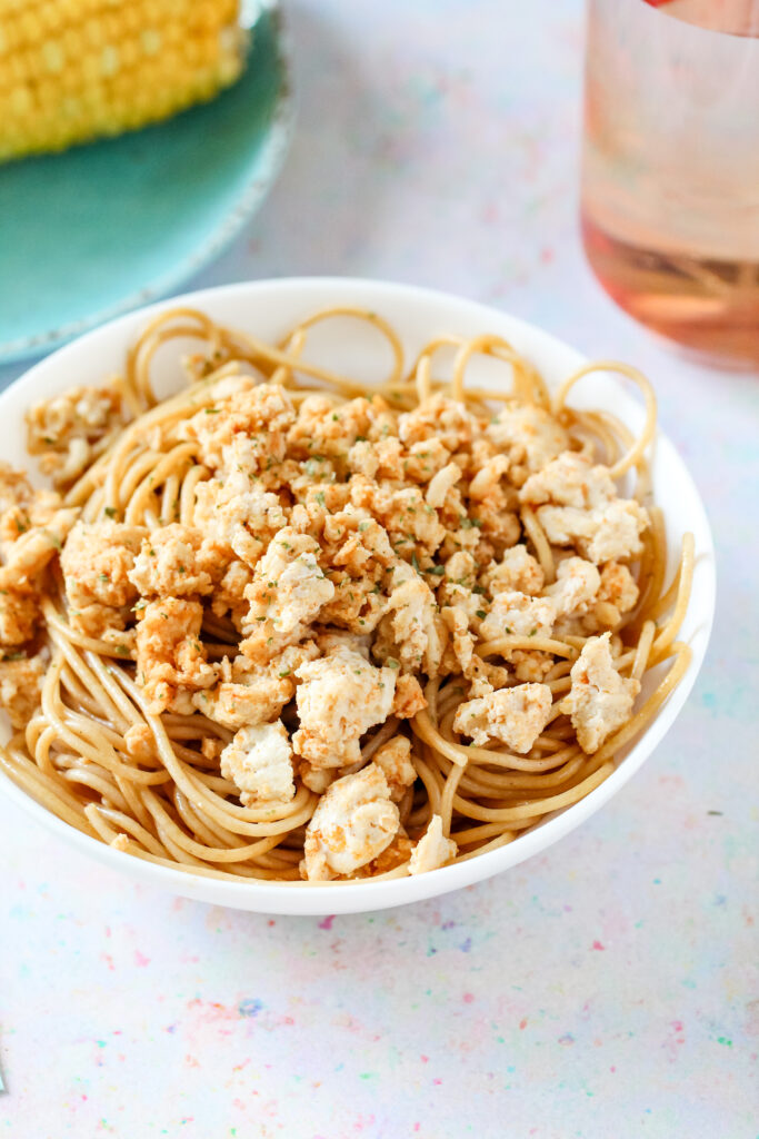 A bowl of seasoned ground chicken breast on top of pasta.