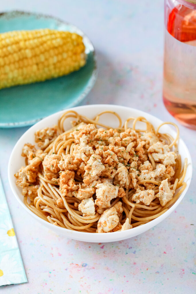 A bowl of seasoned ground chicken breast on top of pasta.