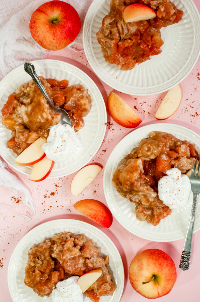 Warm Sweater Weather Caramel Apple Cake topped with gooey caramelized apples and served with whipped cream and fresh apple slices on a pink background.