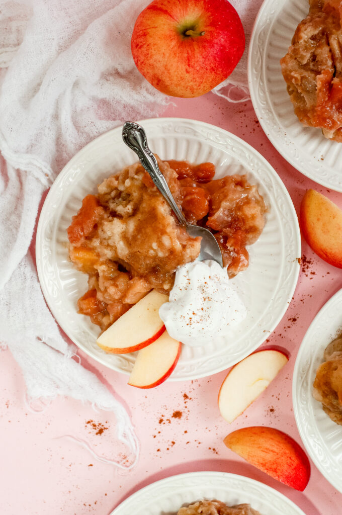 Warm caramel apple cake topped with tender baked apples and served with whipped cream and apple slices — a cozy fall dessert perfect for sweater weather.