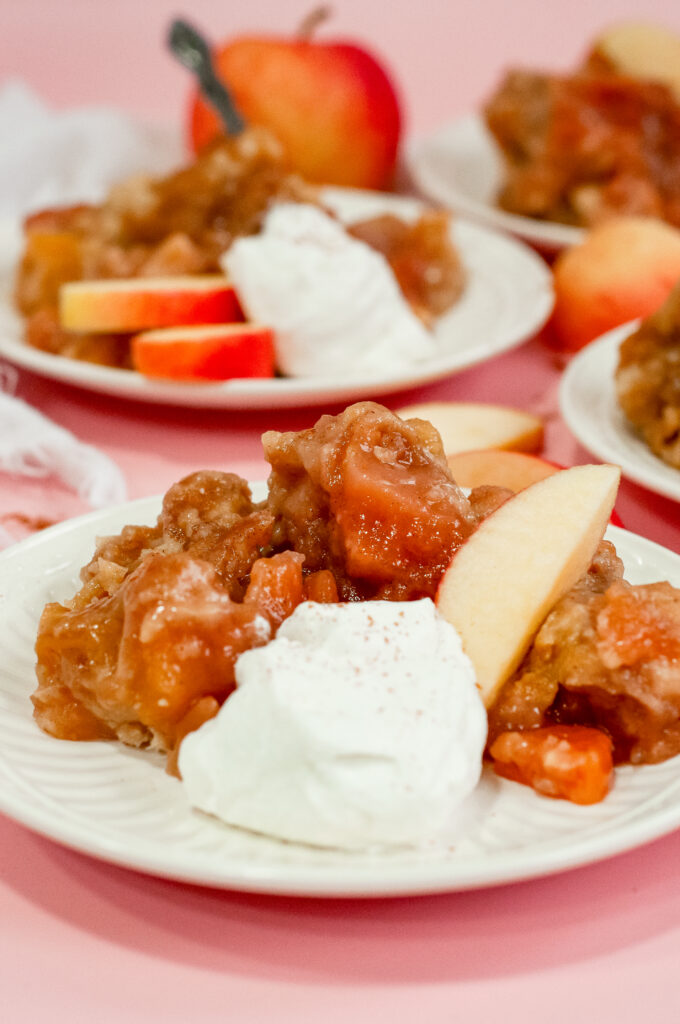 Warm caramel apple cake topped with tender baked apples and served with whipped cream and apple slices — a cozy fall dessert perfect for sweater weather.