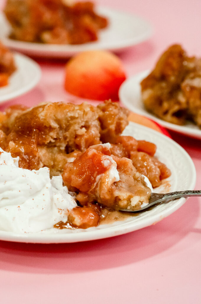 Warm Sweater Weather Caramel Apple Cake topped with gooey caramelized apples and served with whipped cream and fresh apple slices on a pink background.