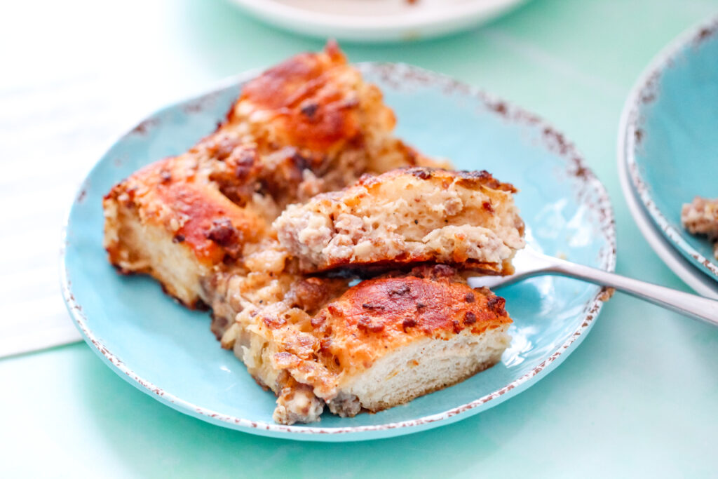 A close-up of savory biscuit and sausage breakfast bake on a blue plate, showing golden brown edges and creamy sausage filling using Pillsbury Grand Biscuits.