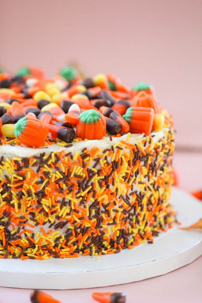 Pumpkin Party Sprinkle Cake covered in orange, yellow, and brown sprinkles and topped with candy corn and candy pumpkins.