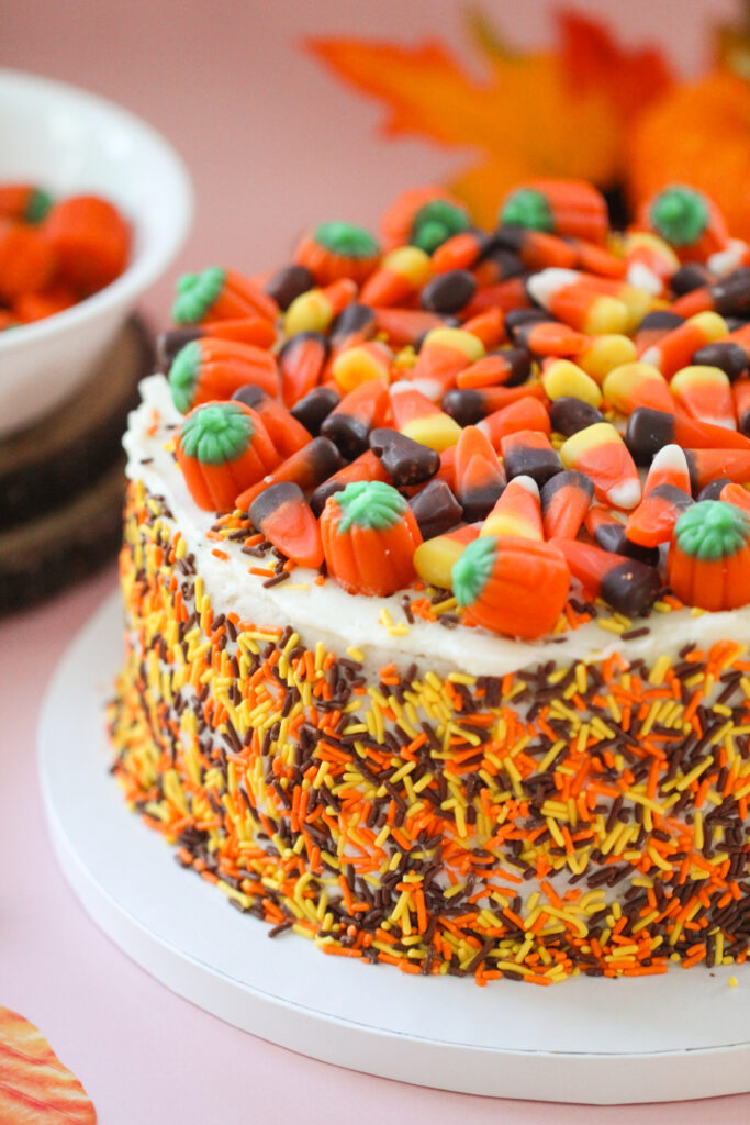 Pumpkin Party Sprinkle Cake covered in orange, yellow, and brown sprinkles and topped with candy corn and candy pumpkins.