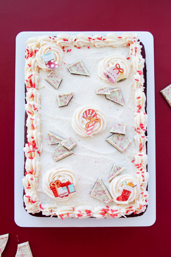 Holiday red velvet cake frosted with creamy white icing and adorned with peppermint candy pieces and Christmas decorations.