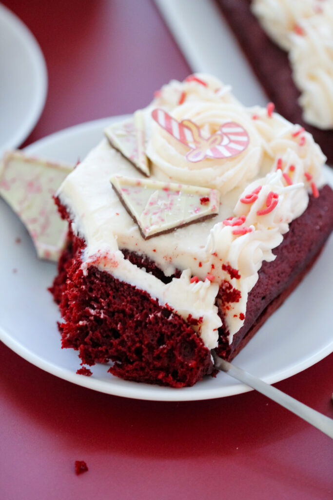 A slice of Red Velvet Candy Cane Cake with white buttercream, peppermint sprinkles, and candy toppings — an easy festive dessert for Christmas.